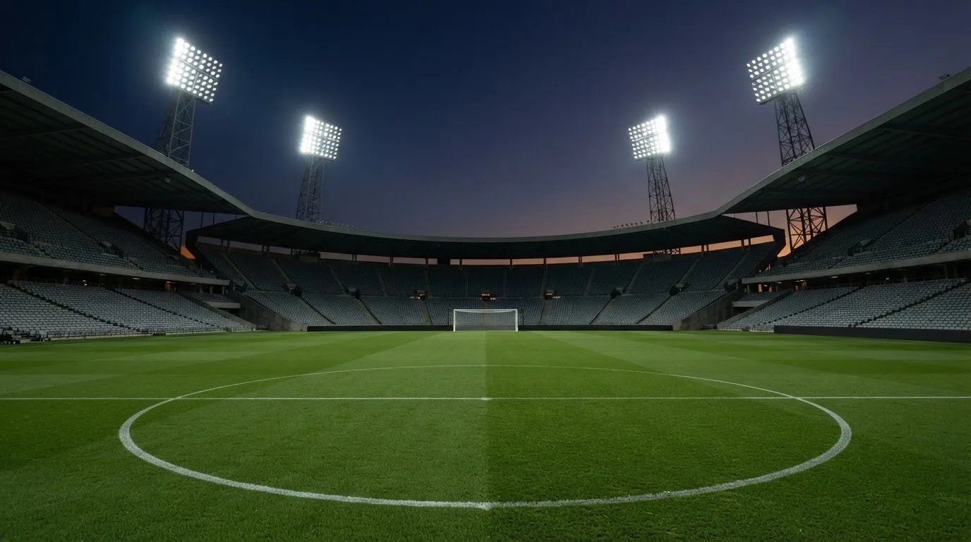 An empty football stadium with floodlight masts at dusk