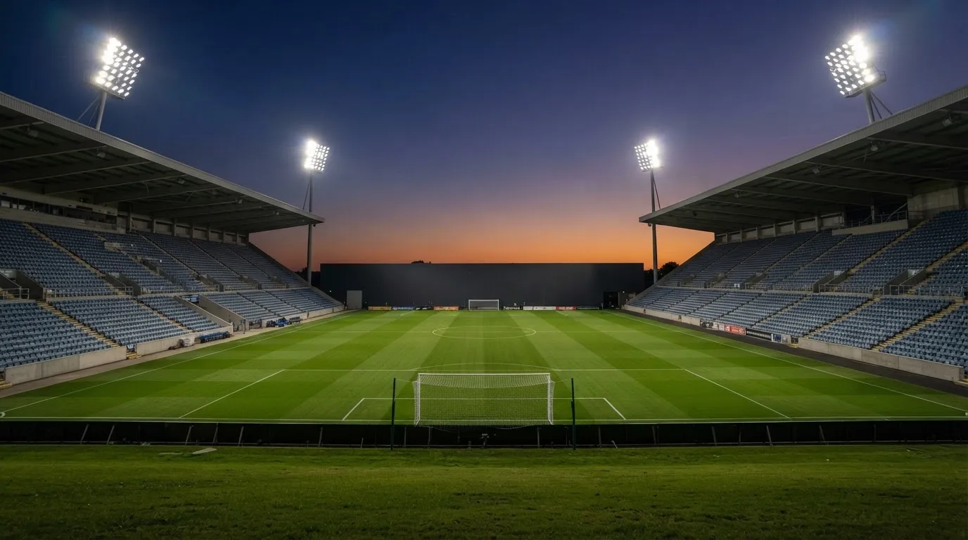 An empty football stadium with floodlight masts at dusk