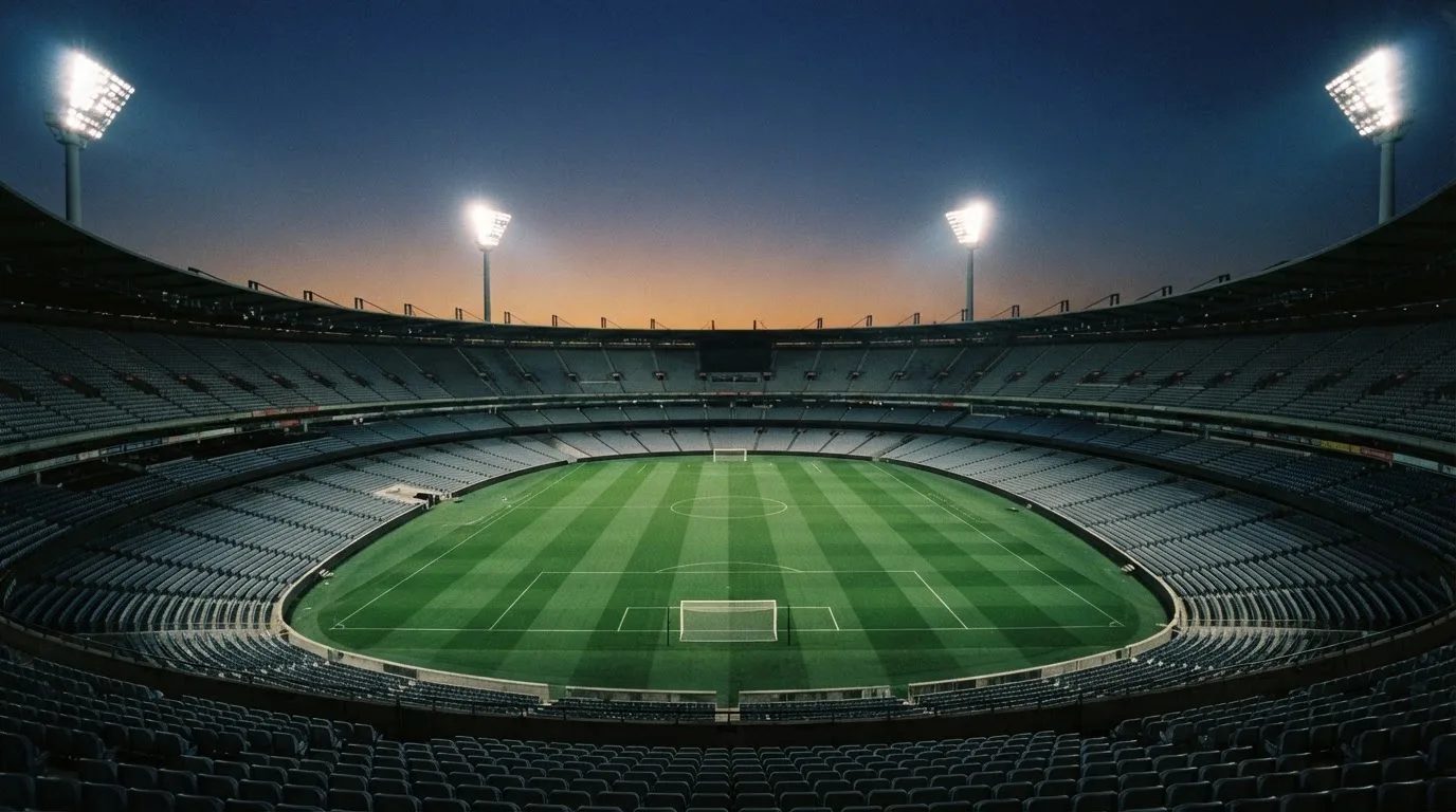 An empty football stadium with floodlight masts at dusk