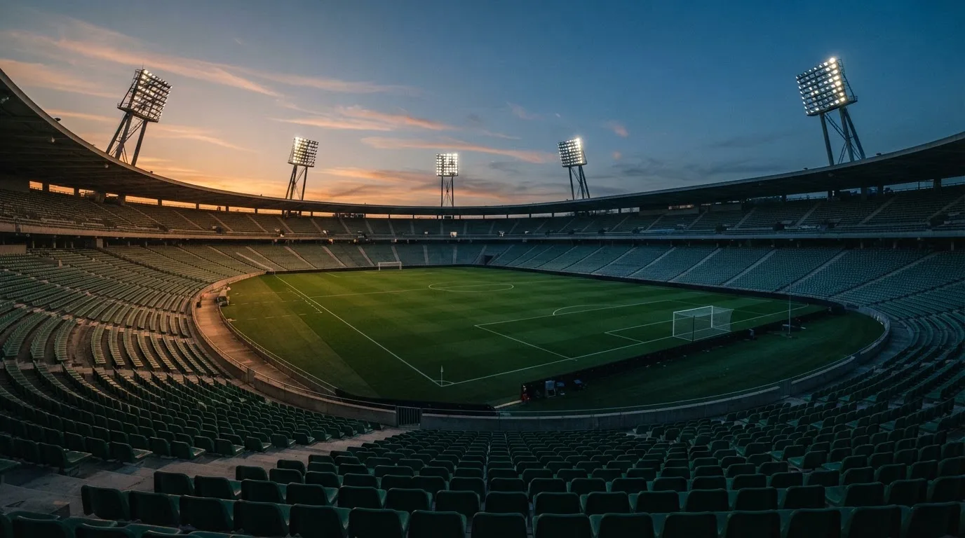 An empty football stadium with floodlight masts at dusk