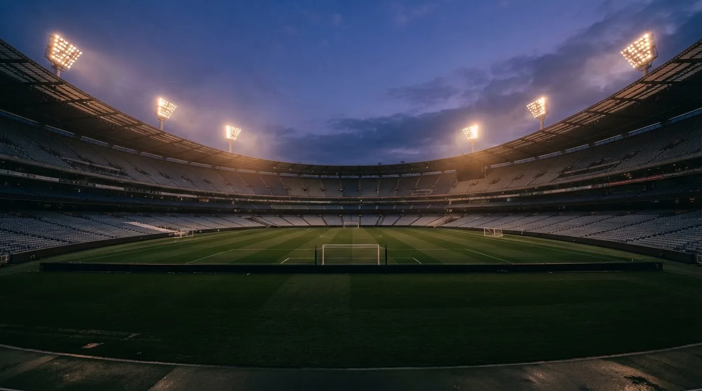 An empty football stadium with floodlight masts at dusk