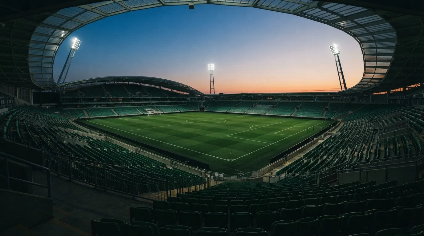 An empty football stadium with floodlight masts at dusk